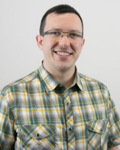 Jonathan Brier smiling with glasses and wearing a green and yellow pocketed shirt